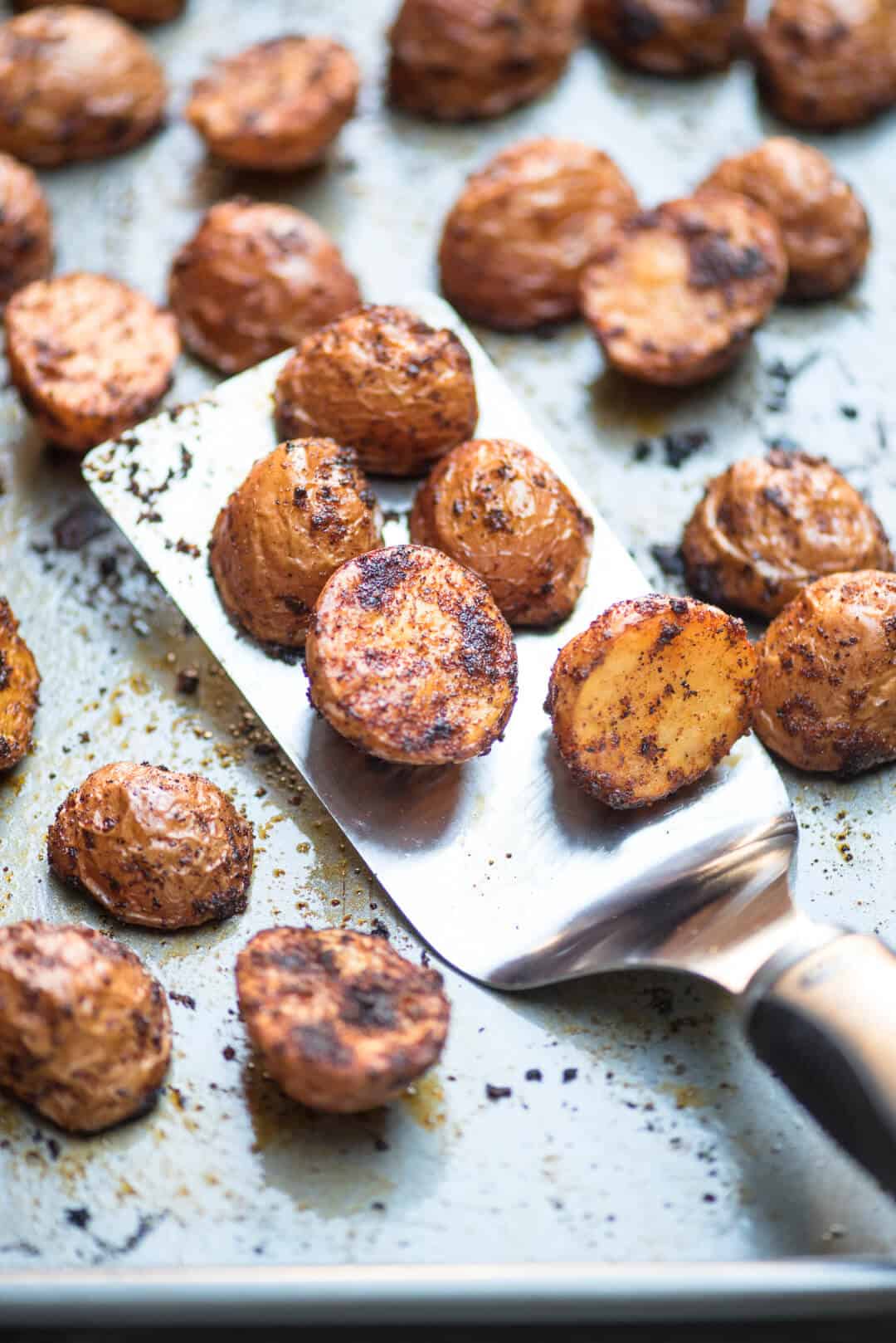 A spatula scoops up some Oven Roasted BBQ Potatoes from a baking sheet.