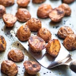 Spiced roasted potatoes on a baking sheet with a spatula.