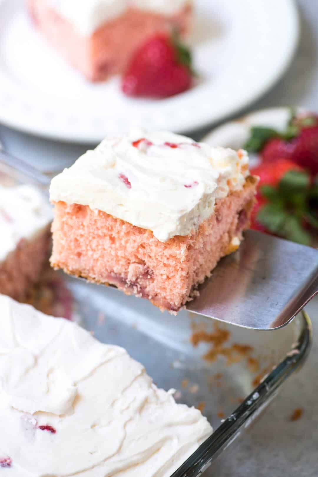 A slice of strawberry cake is lifted with a spatula.