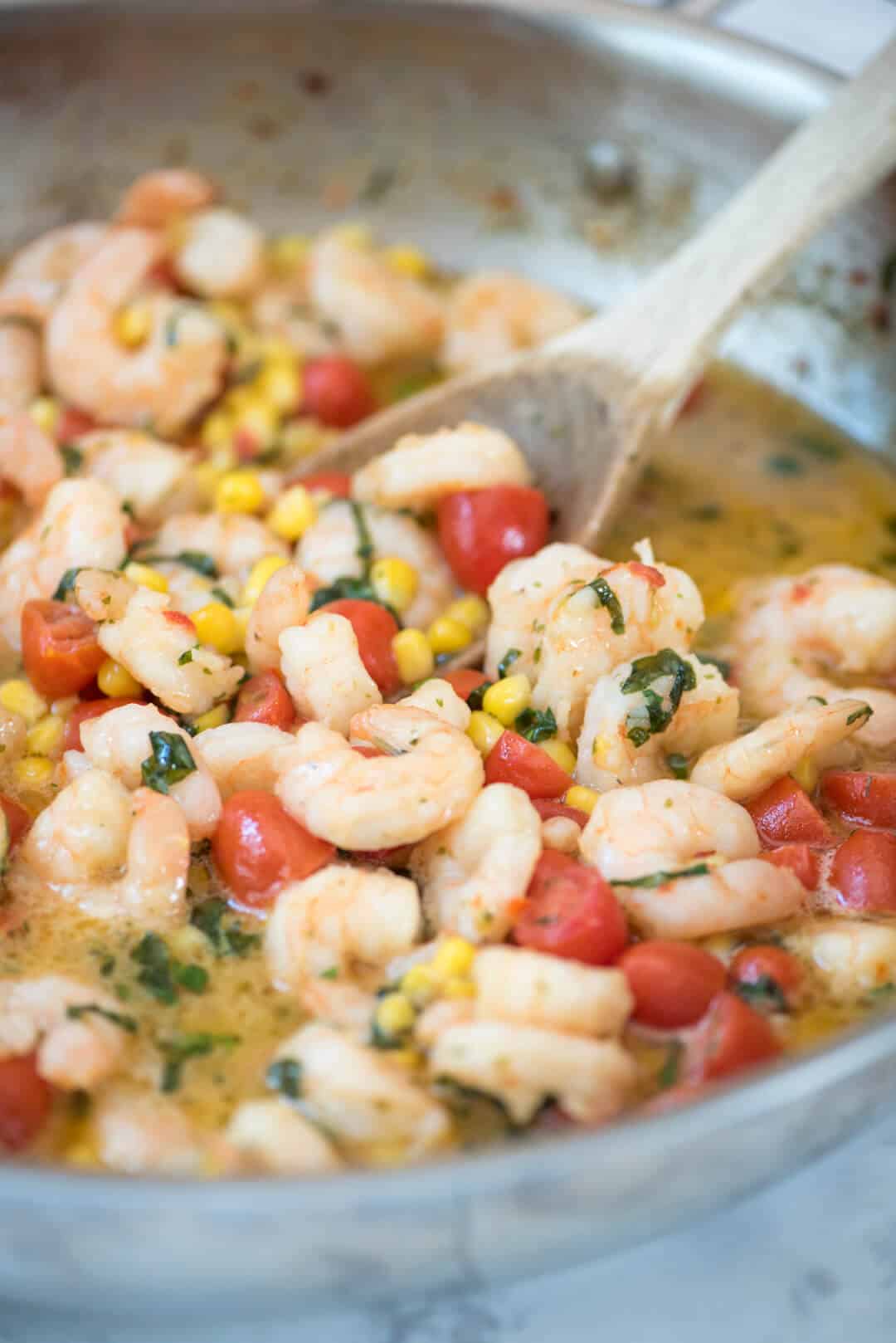 Summer Shrimp Scampi in a skillet being stirred with a wooden spoon.