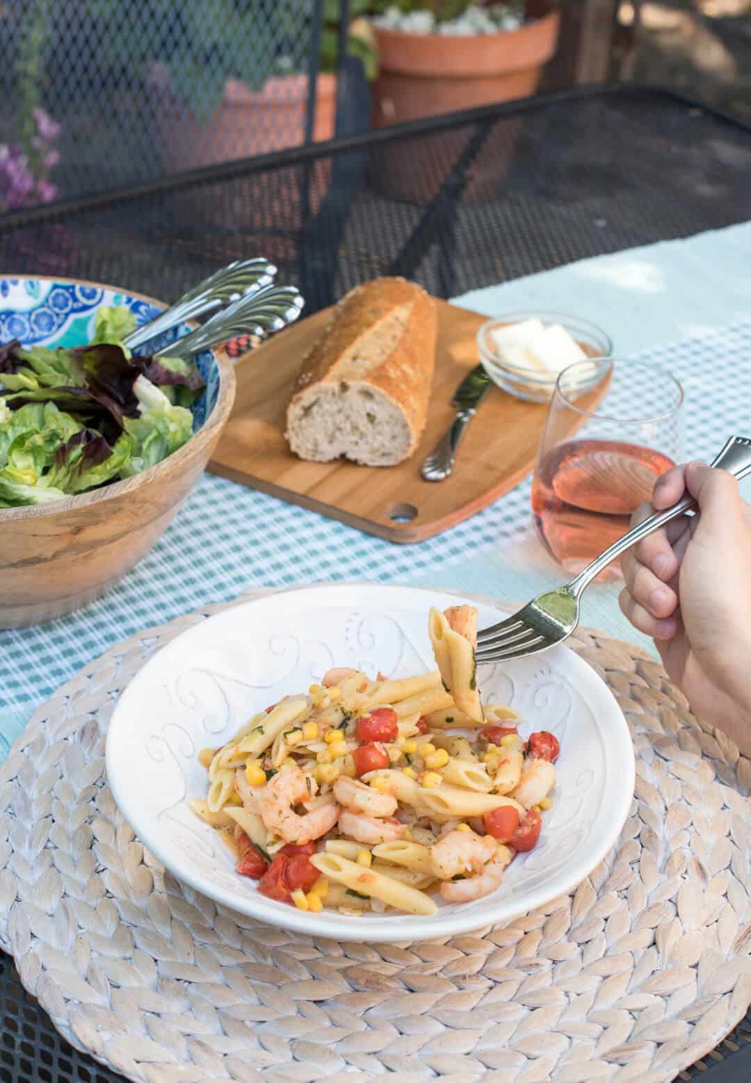 A fork lifts a bite of shrimp scampi with tomatoes and corn on an outside dining table.