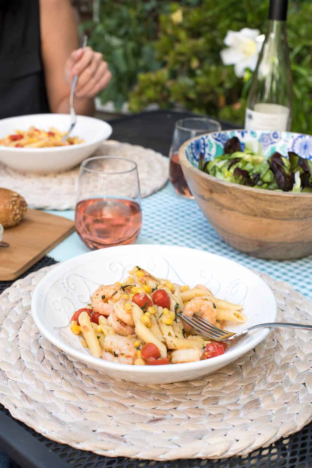 A bowl of pasta with shrimp, tomatoes, and corn on an outside dining table.