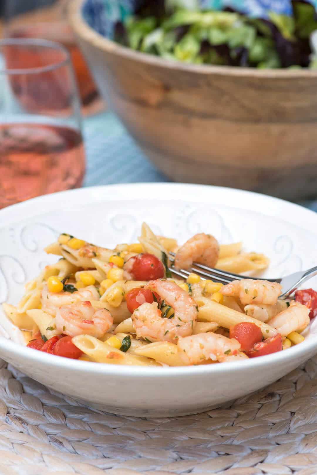 Pasta with shrimp, tomatoes, and corn in a white bowl.