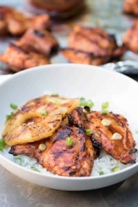 Glazed chicken on rice with a slice of pineapple in a white bowl.