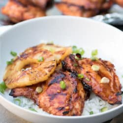 Two pieces of glazed Hawaiian BBQ Chicken and pineapple rings over white rice in a white bowl.