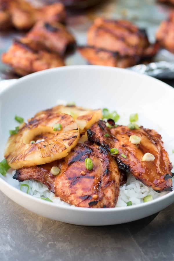 Two pieces of glazed Hawaiian BBQ Chicken and pineapple rings over white rice in a white bowl.