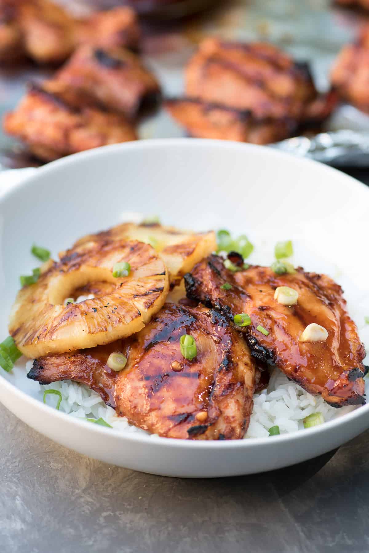 Two pieces of glazed Hawaiian BBQ Chicken and pineapple rings over white rice in a white bowl.