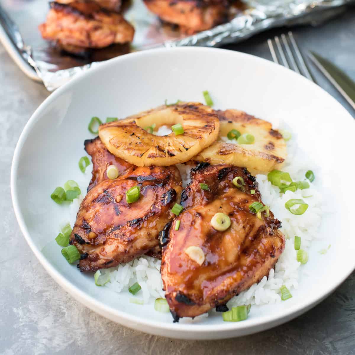 Two pieces of glazed Hawaiian BBQ Chicken and pineapple rings over white rice in a white bowl.