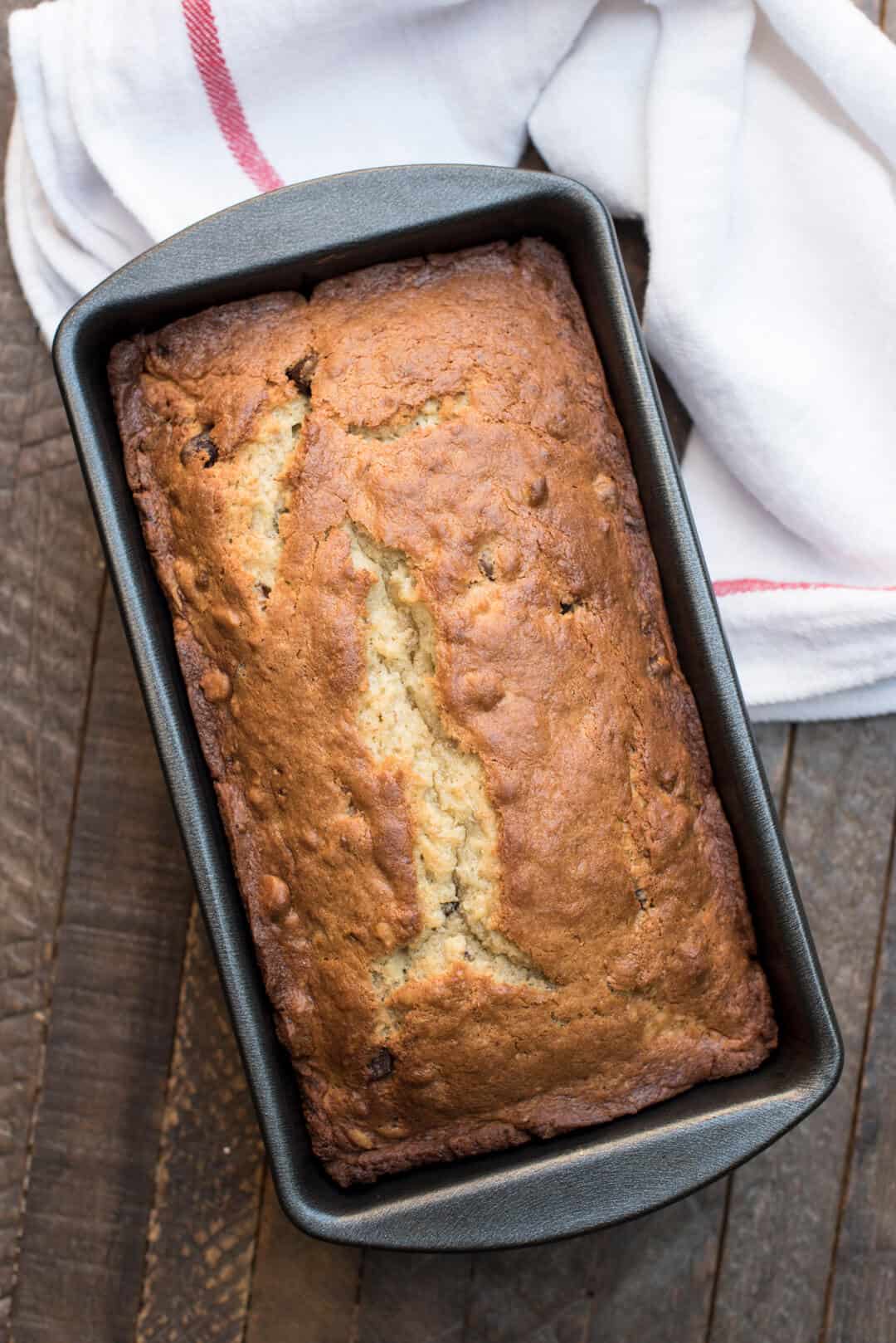 An over the top shot of the banana bread in a loaf pan on a dark wood surface.