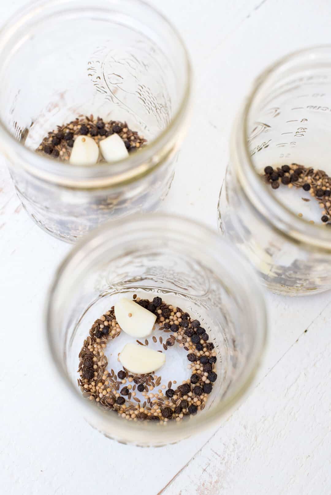 The pickling spices and garlic cloves in the bottom of three empty mason jars.