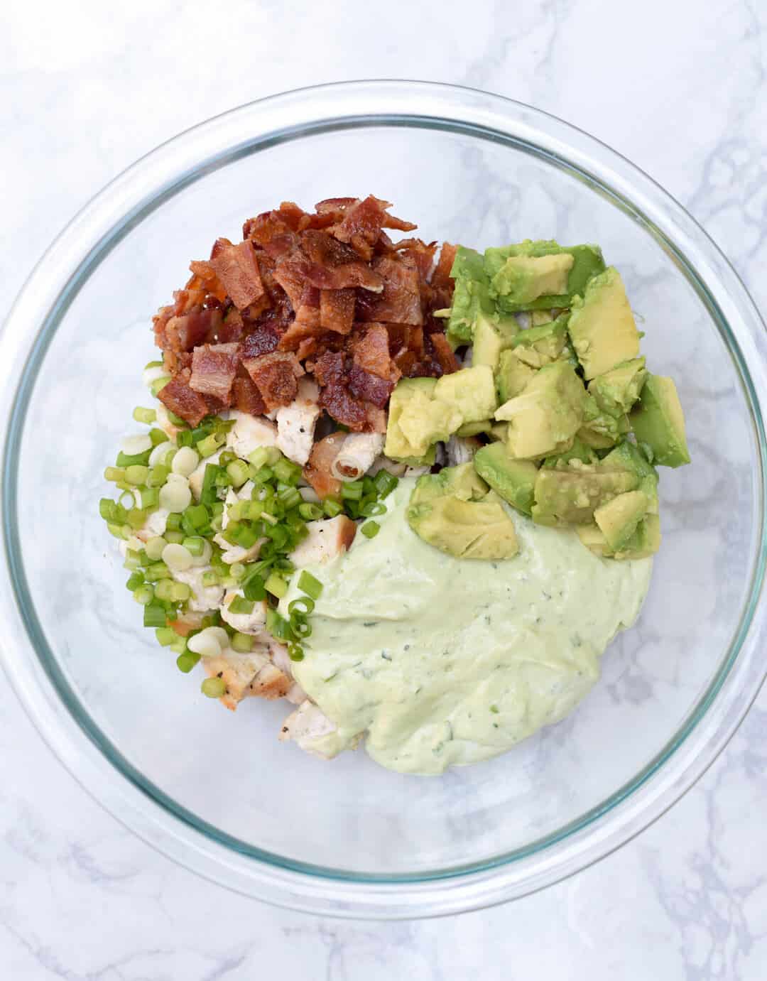 The ingredients for Avocado Bacon Chicken Salad in a glass mixing bowl.