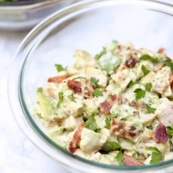 A close up of chicken salad with bacon and avocado in a glass bowl.