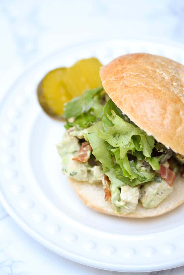 A small sandwich with lettuce on a plate with pickles.