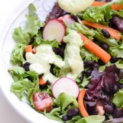 A salad in a bowl topped with a green tinted ranch dressing.