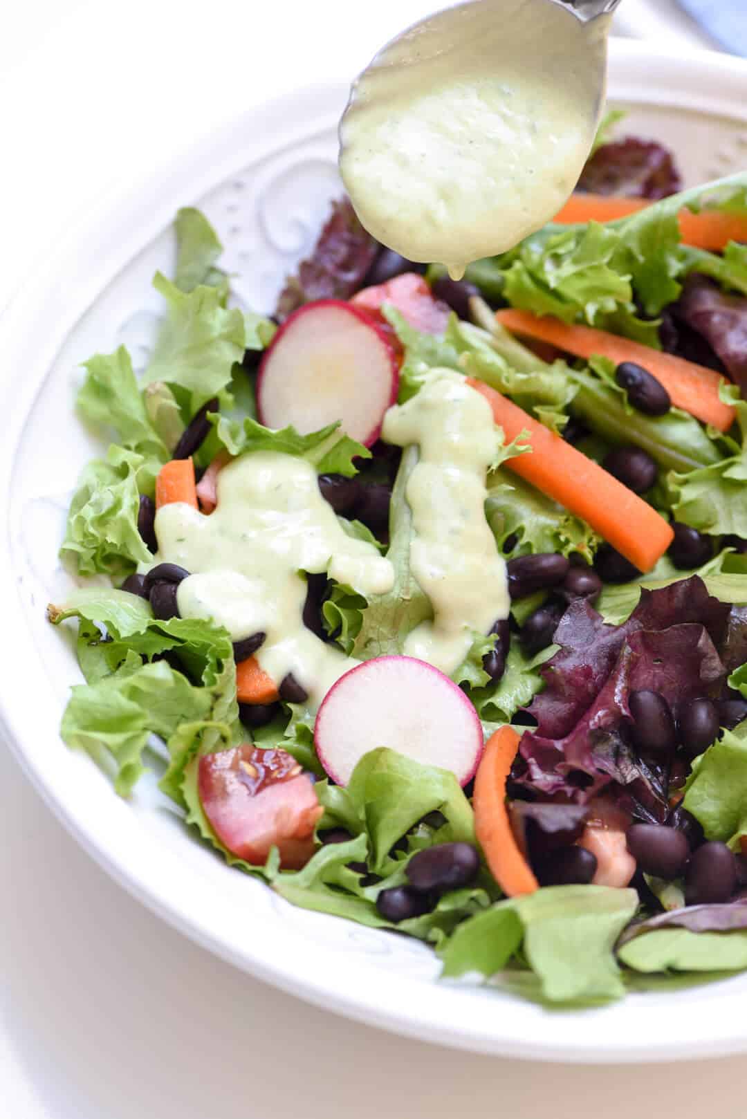 A salad in a bowl topped with a green tinted ranch dressing.