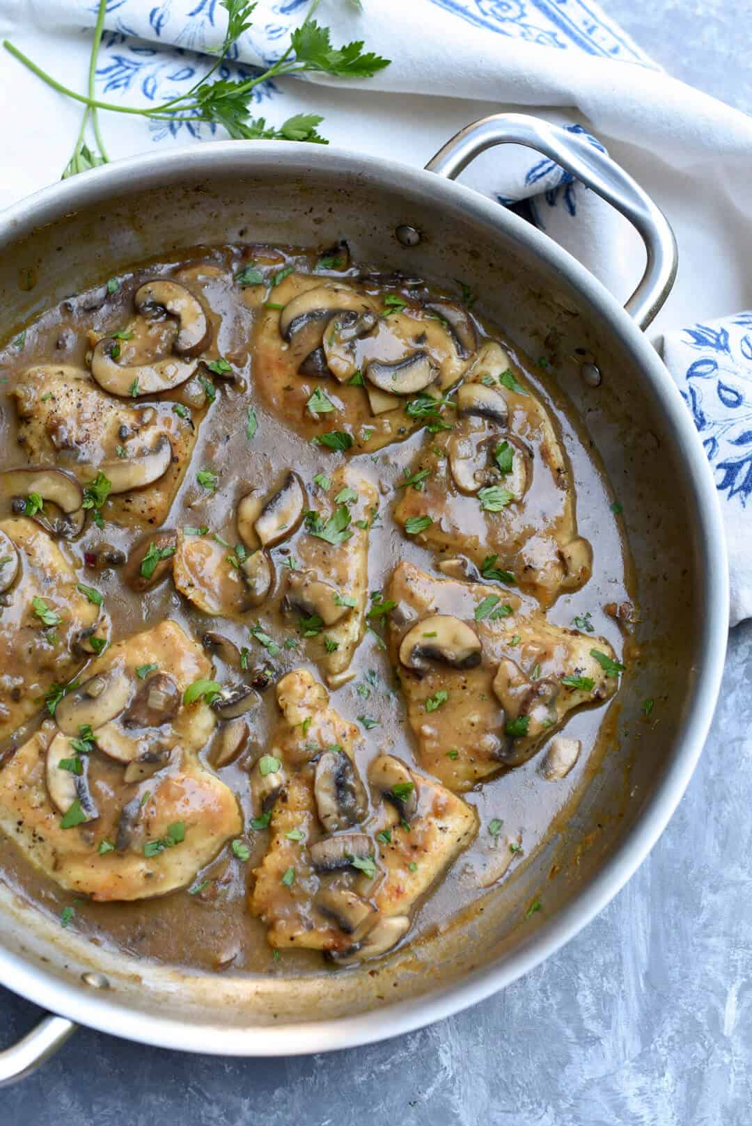 Easy Chicken Marsala in a metal skillet on top of a white and blue kitchen towel.