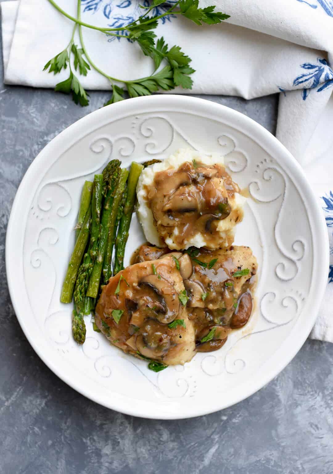 A serving of the finished recipe in a white bowl with asparagus and mashed potatoes.