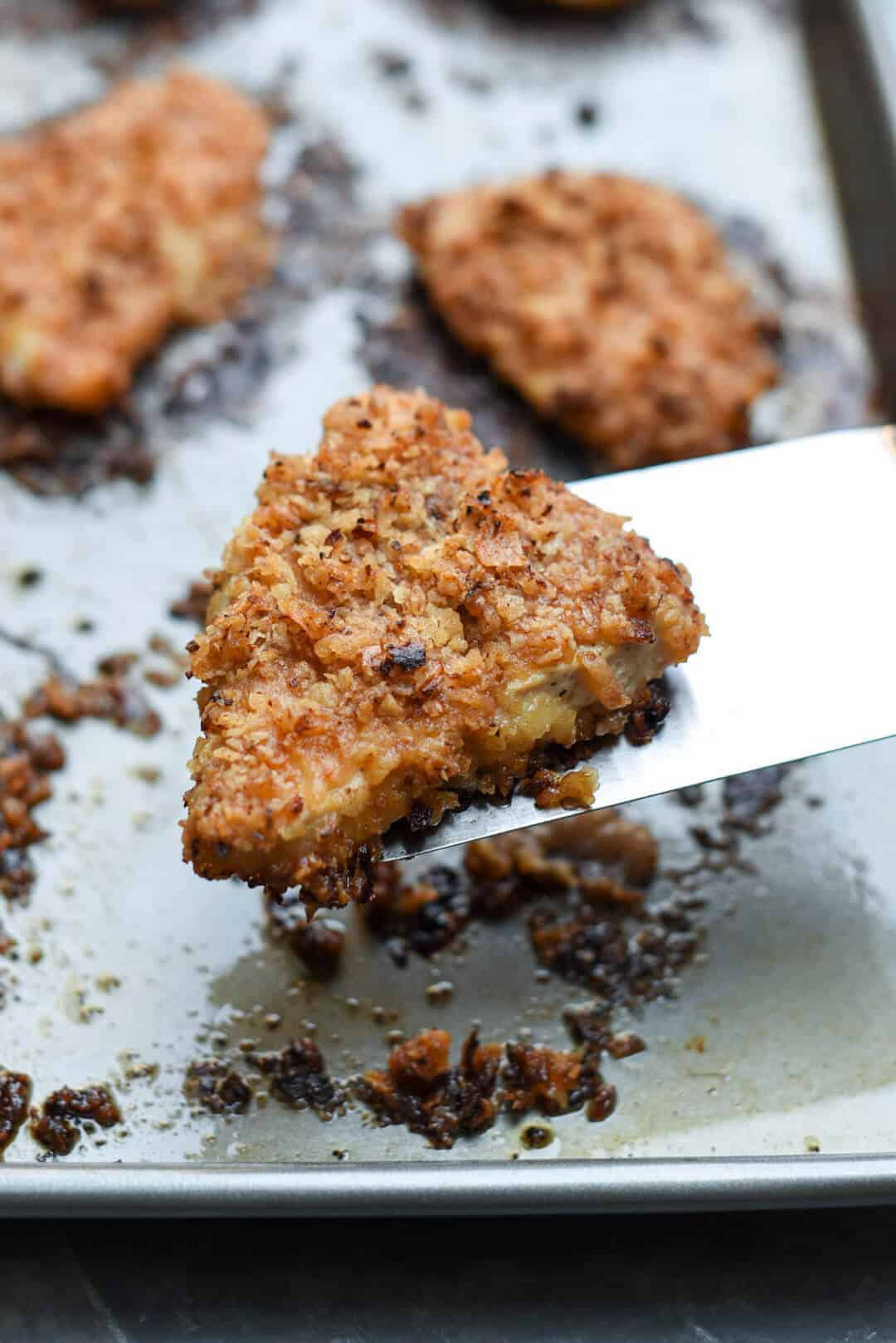 A spatula lifts a piece of Crispy Onion Chicken from a baking sheet.