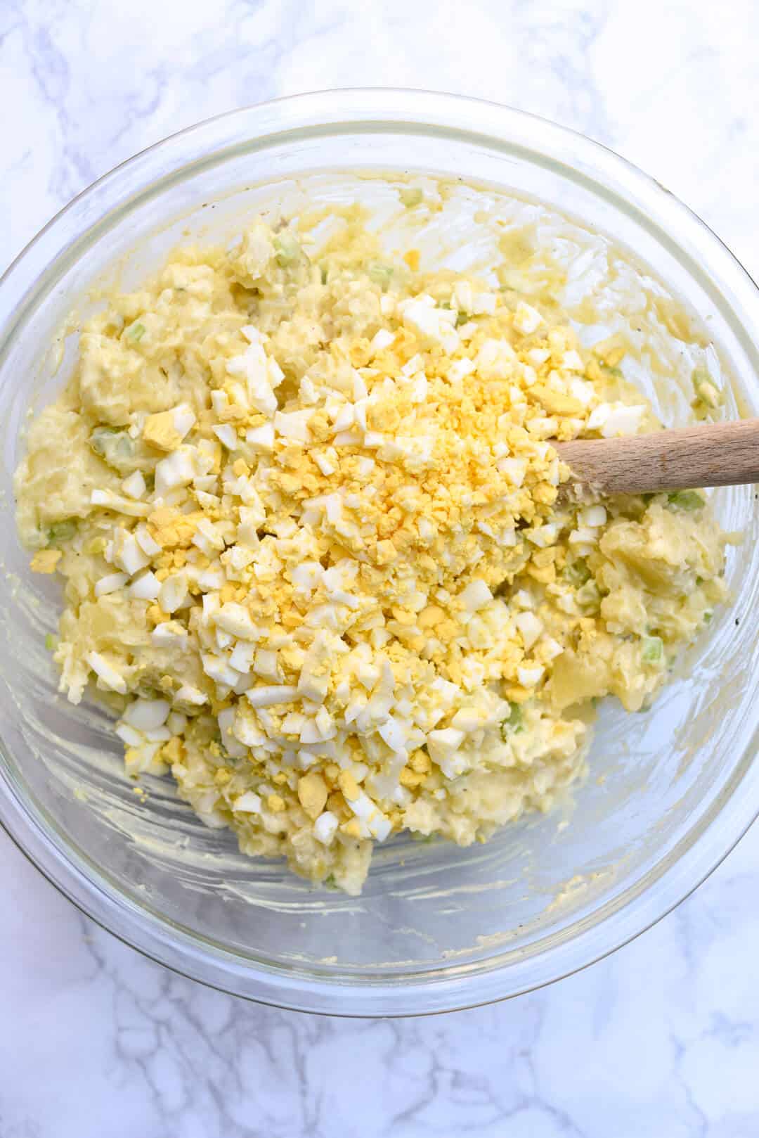 An in process image showing the chopped hard boiled eggs added to the salad mixture in a glass bowl.