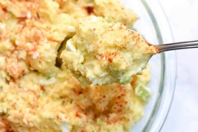 A spoon lifts Potato Salad from a bowl.