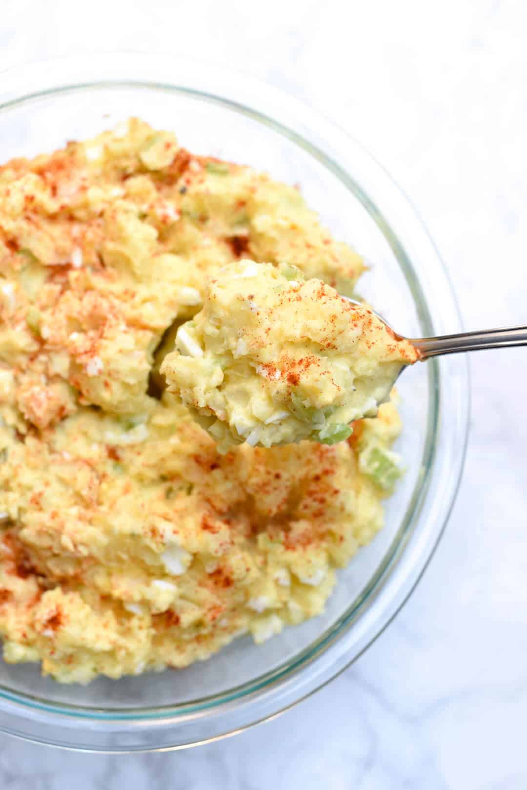 A spoon scoops some of the potato salad from the glass bowl.