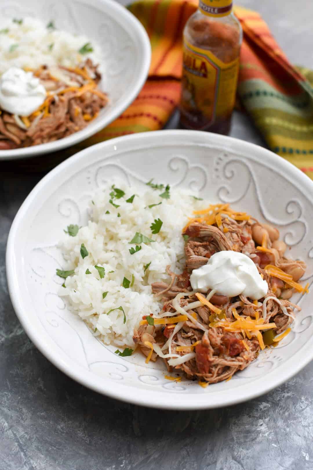 Shredded Mexican Pork and Beans topped with sour cream in a white bowl.
