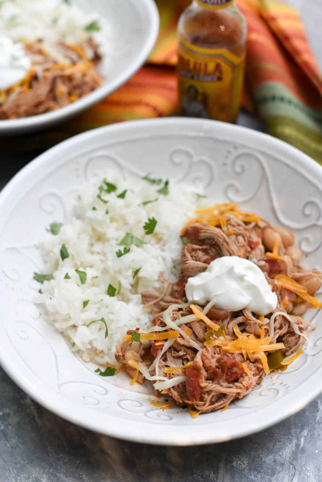Shredded pork and beans topped with cheese and sour cream in a bowl with rice.