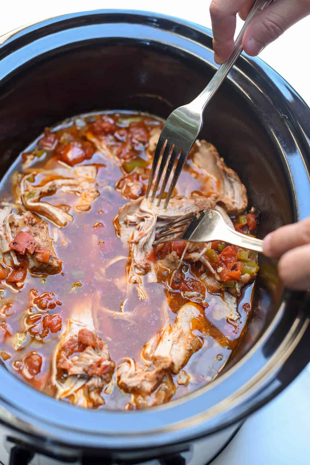 A fork pushes into a tender piece of cooked pork in a slow cooker.