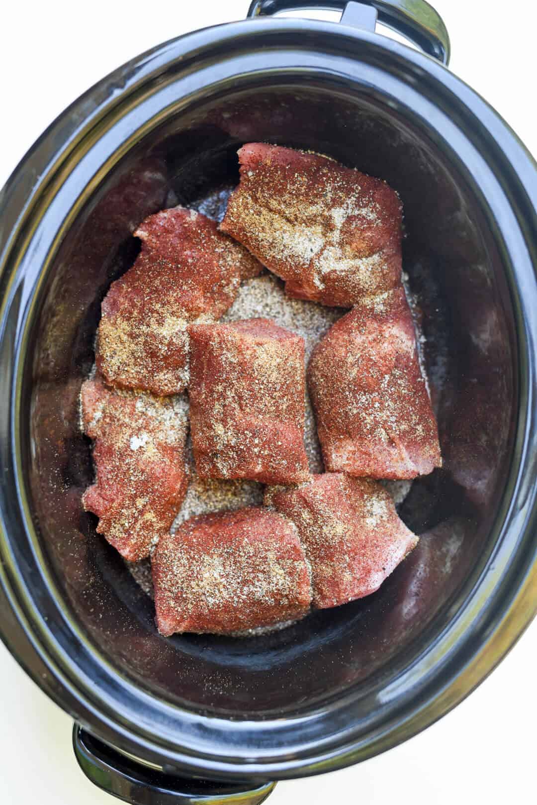 Chunks of seasoned pork in a slow cooker.