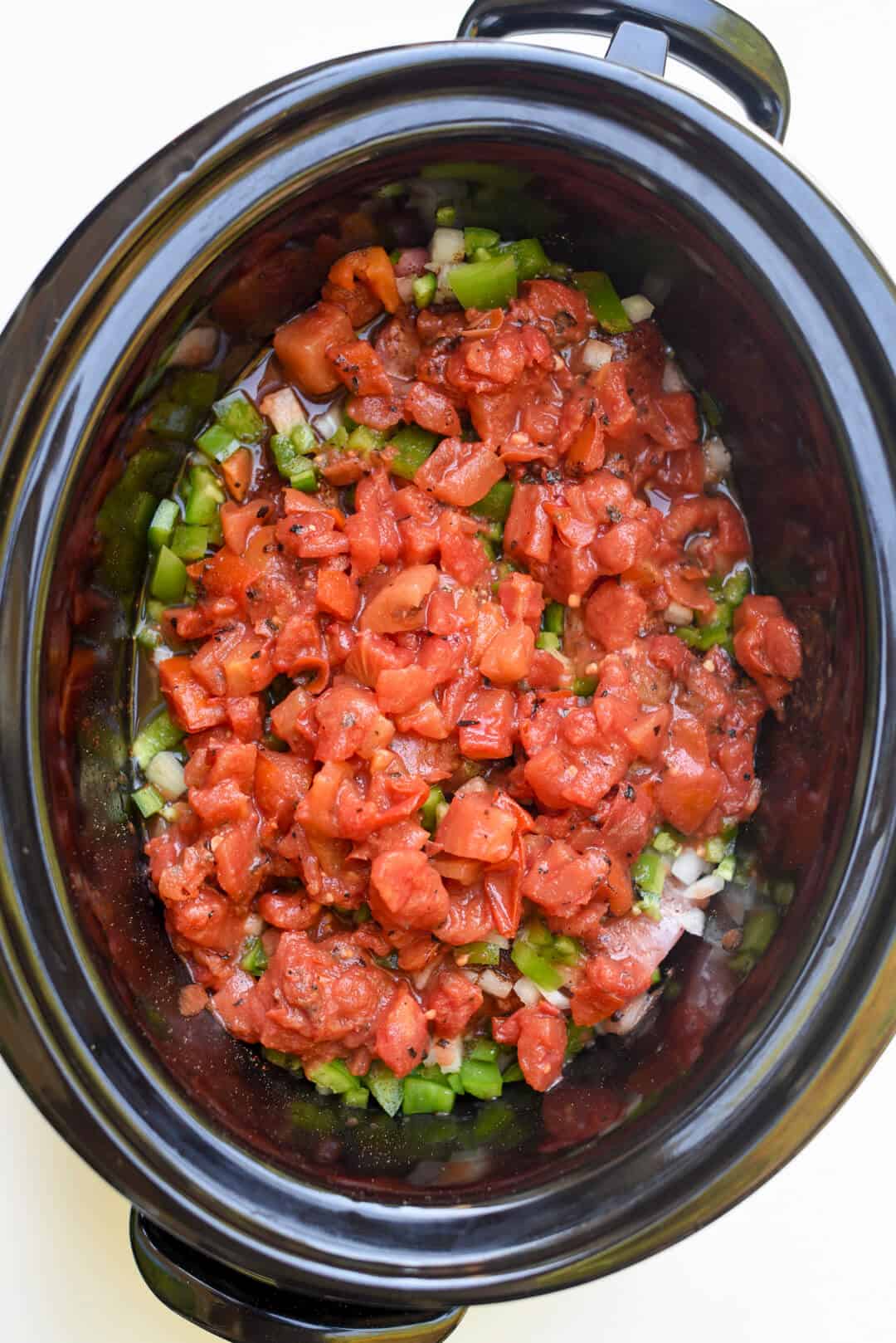 Diced tomatoes on top of pork and vegetables in a slow cooker.