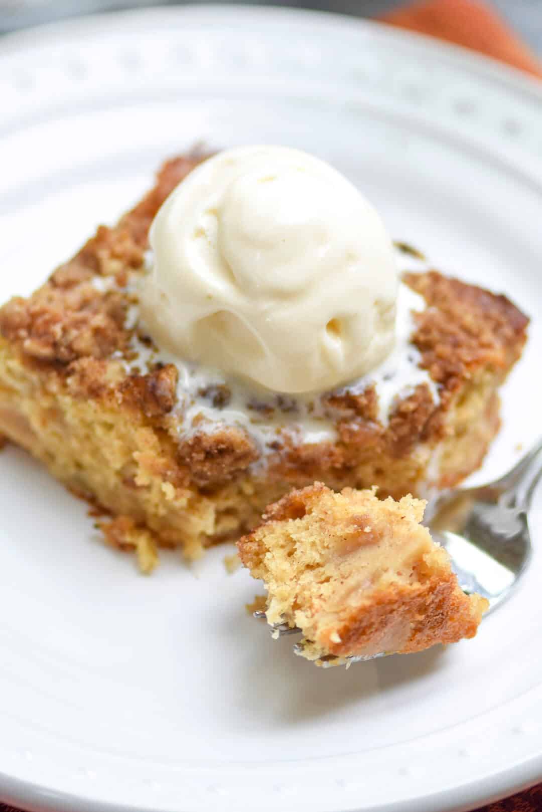 A melting scoop of ice cream on top of as slice of Apple Crumble Cake.