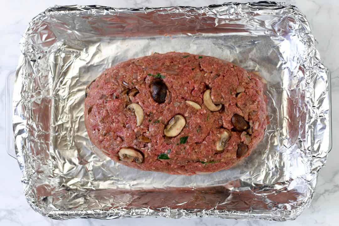 The uncooked meatloaf in a foil lined baking dish.