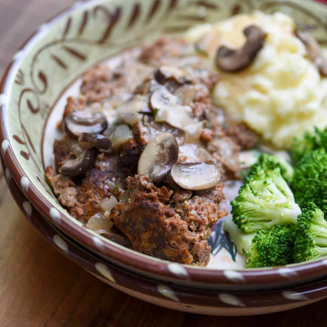A serving of the meatloaf with stroganoff sauce over the top in a bowl.