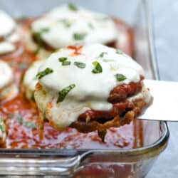 A spatula lifting eggplant parmesan from a baking dish.