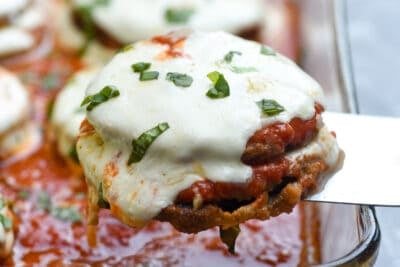 A spatula lifting eggplant parmesan from a baking dish.