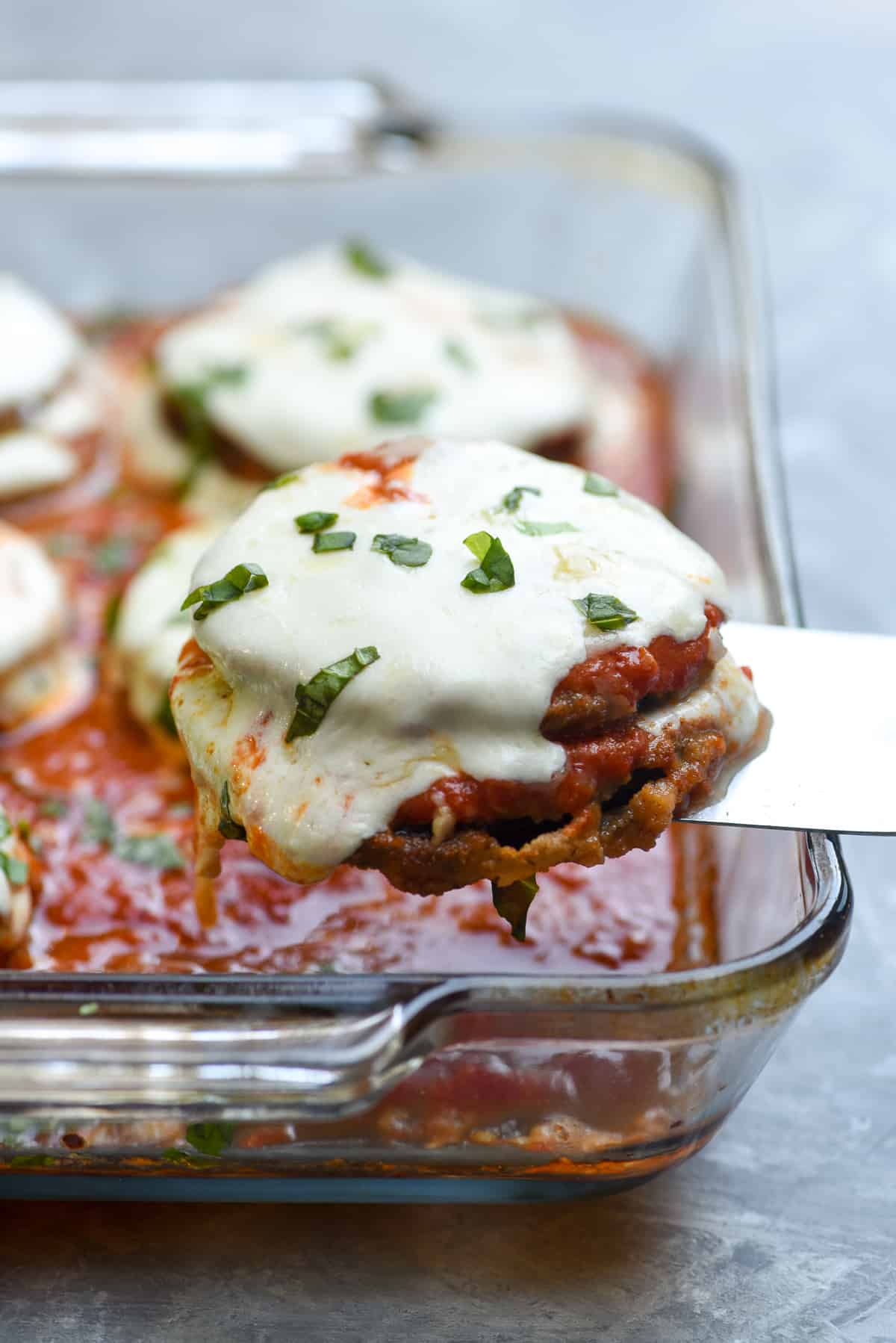 A spatula lifting eggplant parmesan from a baking dish.