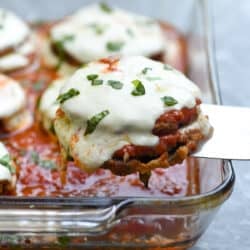 A spatula lifting eggplant parmesan from a baking dish.