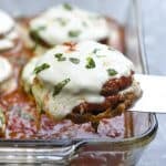 A spatula lifts a piece of eggplant parmesan from a baking dish.