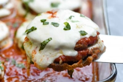 A spatula lifts a piece of eggplant parmesan from a baking dish.