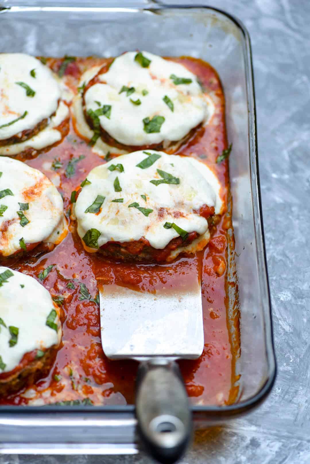 A spatula in a baking dish filled with Baked Eggplant Parmesan.