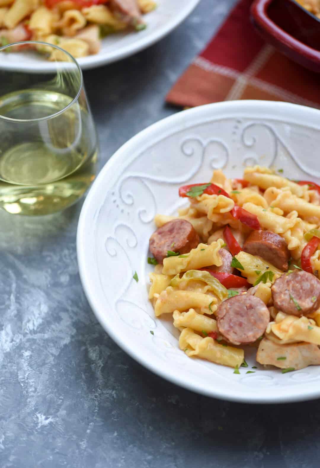 A white bowl filled with Cajun Pasta with a glass of white wine behind it.