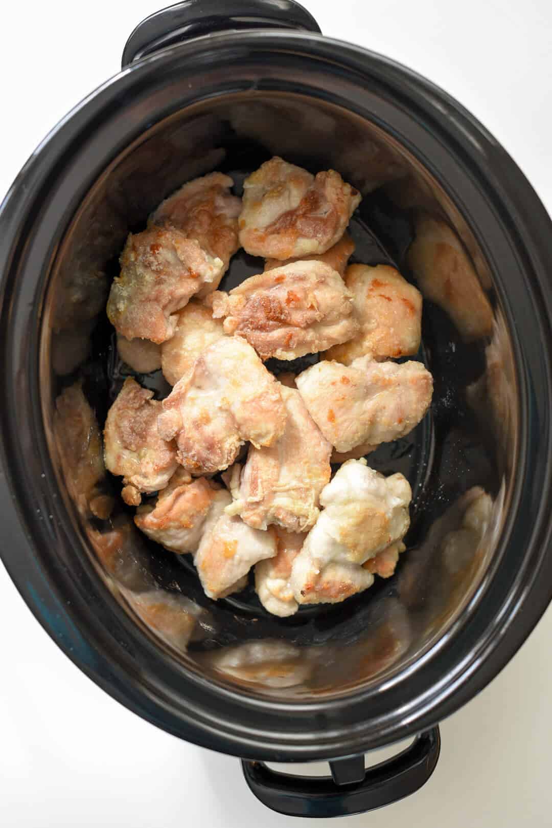 Pieces of chicken in a slow cooker insert.
