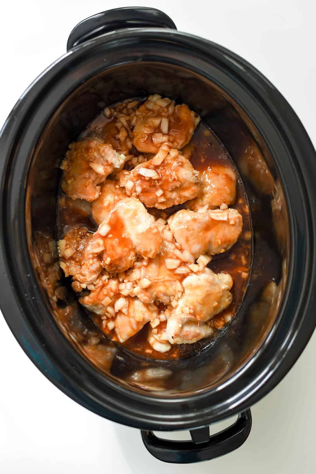 Sauce is poured over the top of the chicken in the slow cooker.