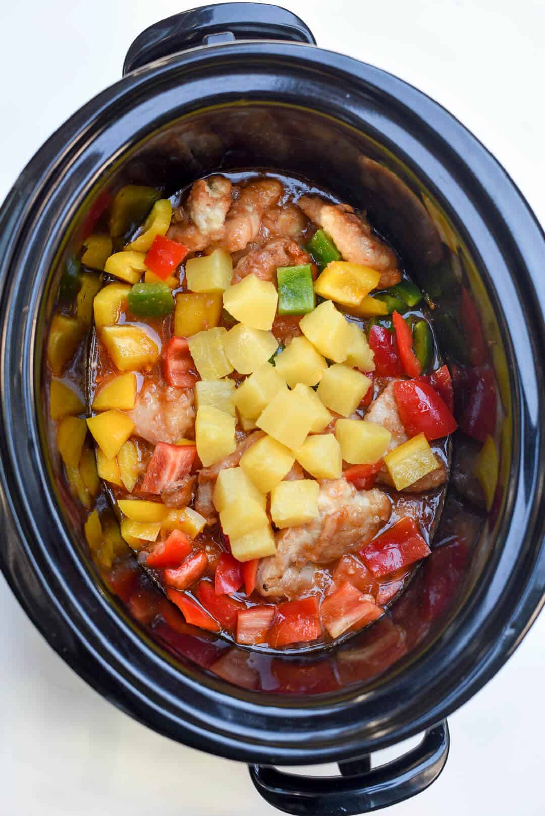 Chunks of pineapple are added to the slow cooker.