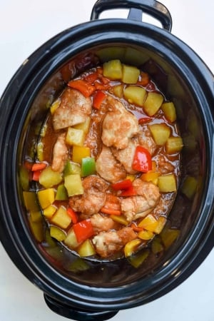 A slow cooker filled with sweet and sour chicken shot from over the top.