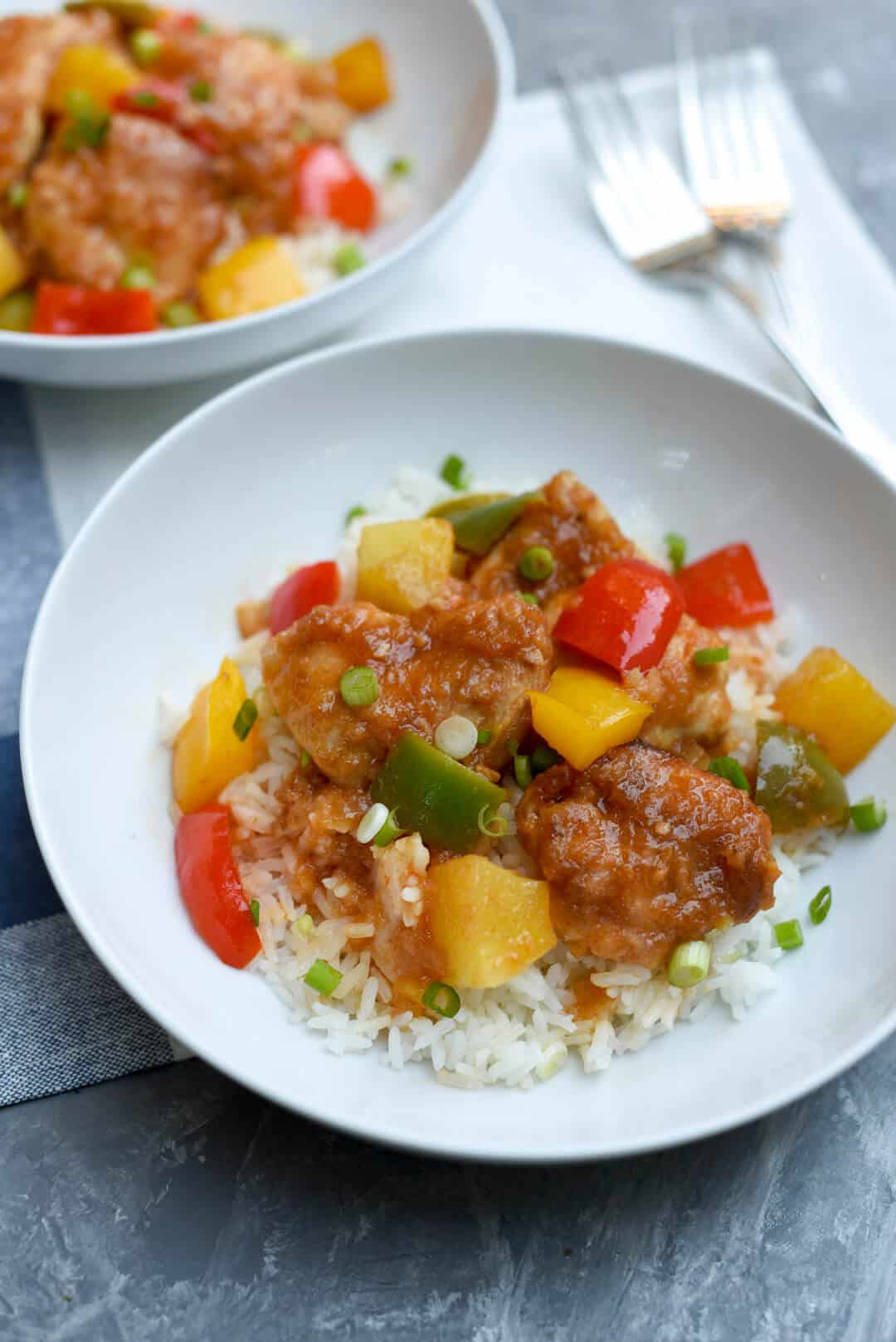 A bowl filled with small pieces of glazed chicken and bright colored vegetables.