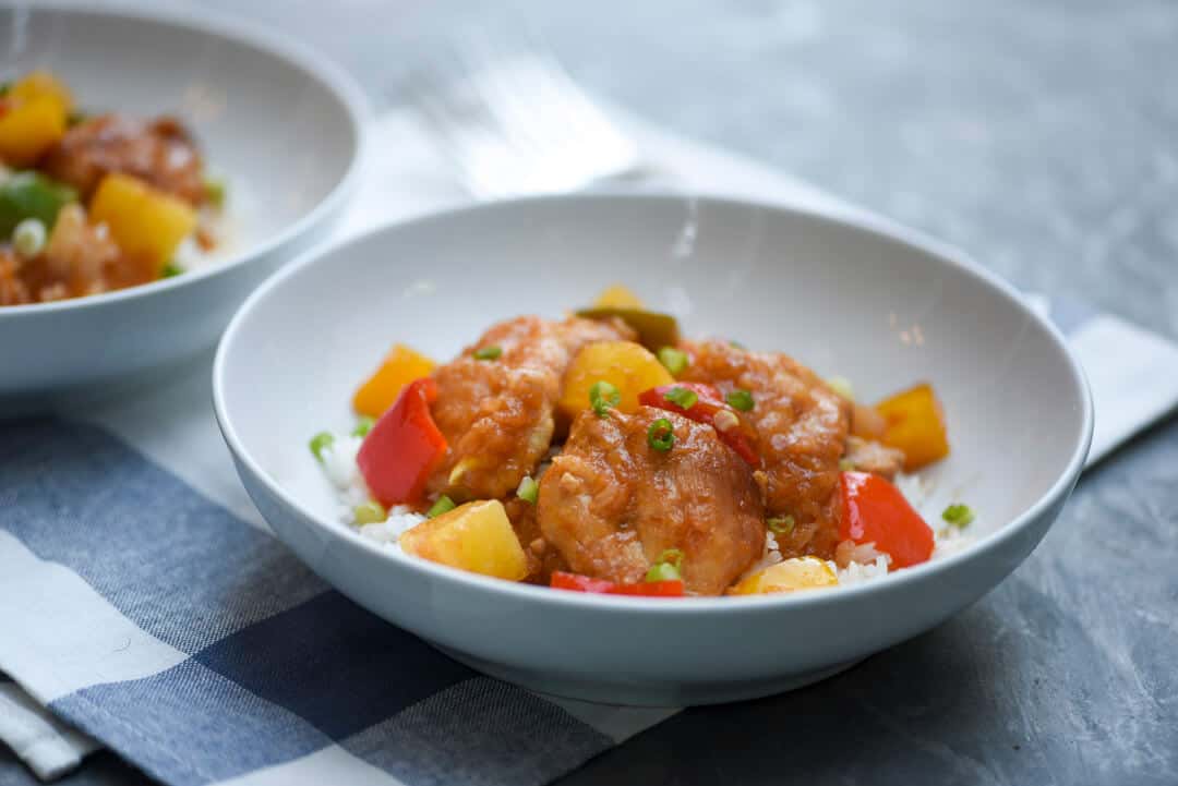 Slow Cooker Sweet and Sour Chicken in a white bowl on a blue and white cloth.