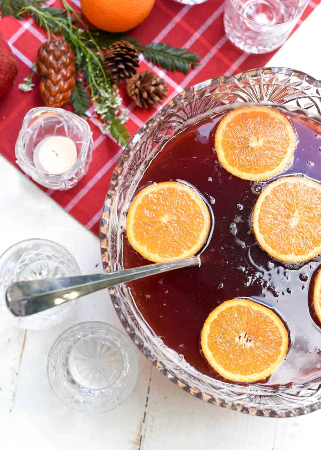 Orange slices float on the surface of the red punch in a punch bowl.