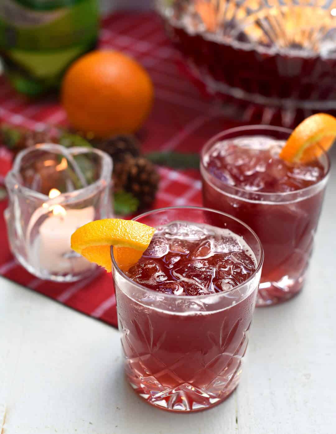 Two glasses of Sparkling Pomegranate Vodka Punch garnished with orange slices near a red cloth.