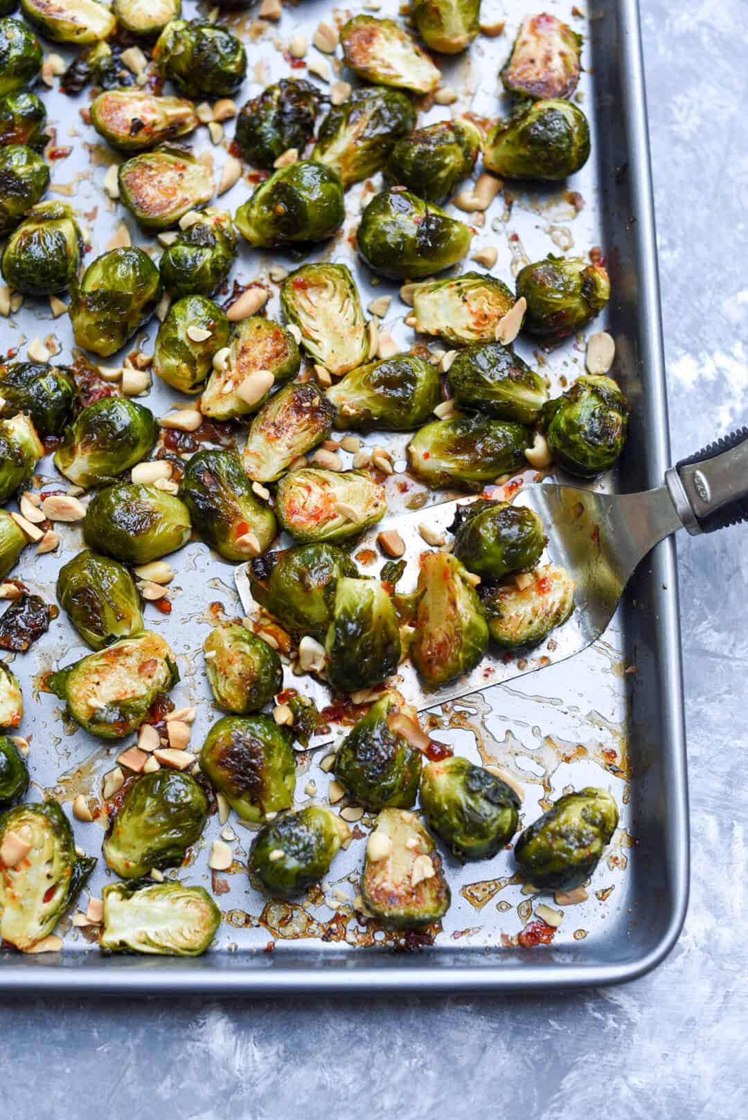 A spatula lifts some of the Brussels sprouts from the baking sheet.